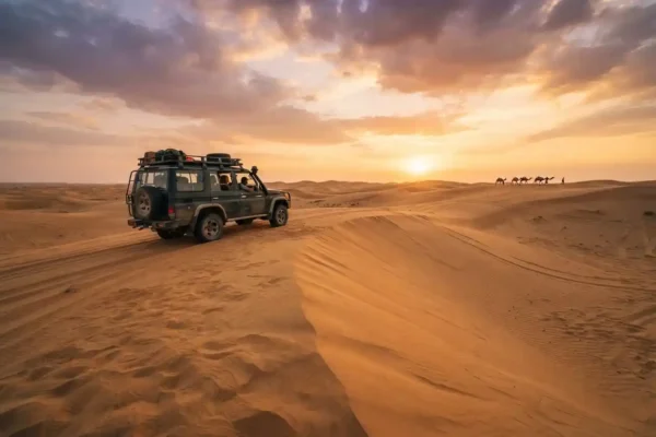 Golden Dubai desert dunes and safari vehicle at sunset